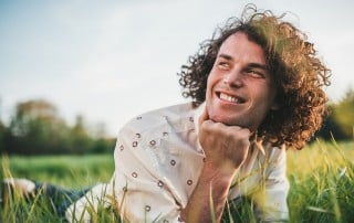 young man with bushy, curly brown hair lays in green grass