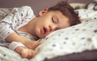 little boy laying in bed on his side suffering from sleep apnea