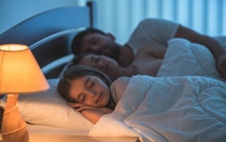 young child sleeps in bed next to her parents, all peacefully