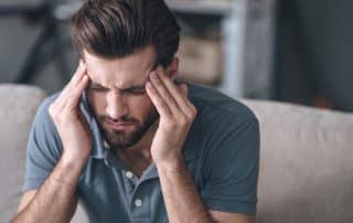 man with TMJ pain sitting on couch trying to massage forehead for relief