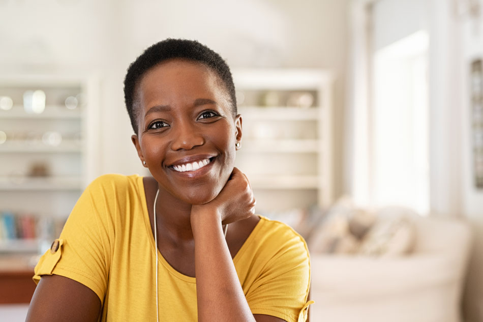 A short-haired woman wearing a yellow shirt sitting and smiling